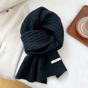 Close-up of thick black knit scarf texture with a white logo label on a cozy background
