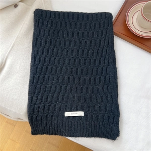 Detailed shot of black waffle knit wool scarf with white branded woven label