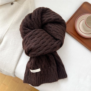 Close-up of thick dark brown knit wool scarf with brand label on a cozy white surface