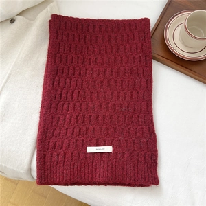 Detail of dark red wool blend knitted scarf with textured check pattern and brand label