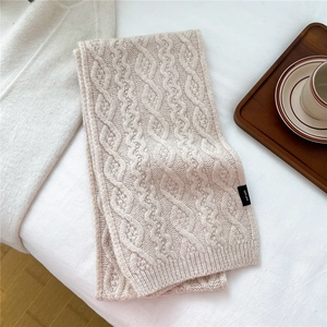 Detail of cable-knit texture and 100% wool label on beige wavy knitted winter scarf