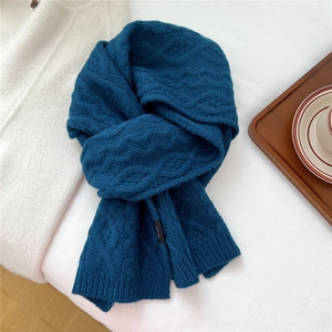 Detailed cable knit pattern on a thick dark blue wool scarf in a cozy winter setting