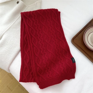 Detail of red cable knit wool scarf showing thick texture and 100% wool material tag