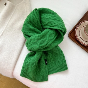 Detail of green cable-knit wool scarf showing 100% wool label and thick texture