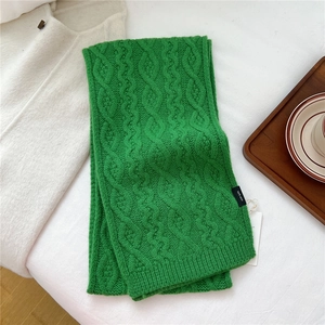 Detailed view of green cable knit wool scarf featuring a 100% wool label and soft texture
