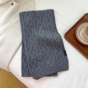 Detail of dark grey wool scarf showing thick cable knit texture and 100% wool label