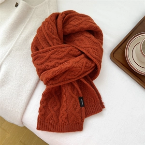 Close-up of caramel orange cable knit wool scarf showing thick texture and 100% wool tag