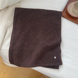 Detail eines weichen dunkelbraunen Wollschals mit Logo-Plakette aus Metall auf Textur