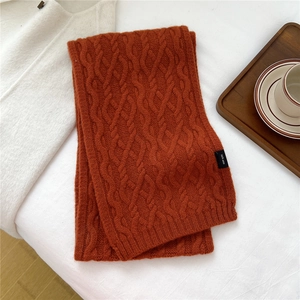 Detail of burnt orange cable knit wool scarf with 100% wool material label and soft texture