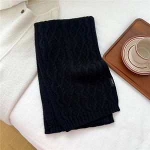 Detail of cable knit wool scarf in black with 100% wool label on fabric