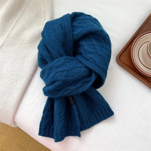 Detail of dark blue cable-knit wool scarf with thick texture on white linen background
