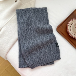 Detailed close-up of dark grey cable-knit wool scarf showing 100% wool label texture