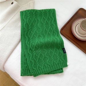 Detail of 100% wool label on green cable-knit scarf showing premium texture and material