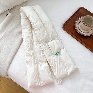 Detail of white quilted down scarf with woven brand tag on a soft bed setting