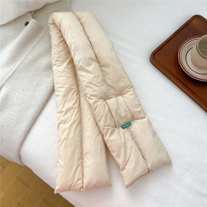 Detail of light beige puffy scarf with SUNEY woven label on cozy knitted background