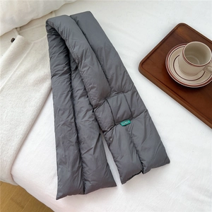 Detail of dark grey quilted down scarf featuring a green brand tag on white fabric
