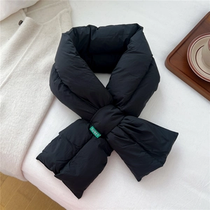 Flat lay of a black quilted down scarf with green logo tag on a white fabric surface
