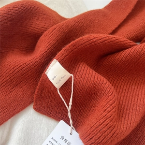 Close-up of 100% wool knitted scarf in terracotta with ribbed texture and fabric label