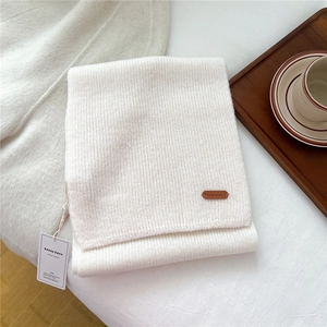 Detail of white knit wool scarf showing soft texture, leather logo, and brand tags
