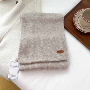 Detailed macro view of oatmeal knit wool scarf with premium leather logo patch