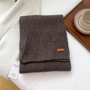Detail of warm brown knit scarf with leather brand label on soft aesthetic background