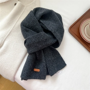 Detailed close-up of dark grey chunky knit wool scarf with premium leather brand label