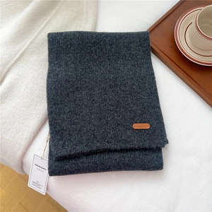 Detail of dark grey knit wool scarf featuring a premium leather logo tag on fabric