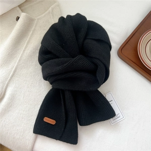 Close-up of black ribbed knit scarf featuring a brown leather patch and woven texture