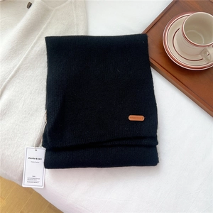 Close-up of black knitted wool scarf featuring leather logo patch and brand tag