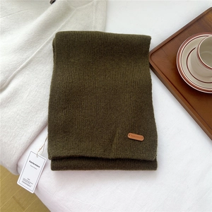 Detail of olive green knitted wool scarf with leather brand tag on a cozy background