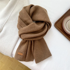 Macro detail of dark camel knit scarf texture with leather tag on white surface