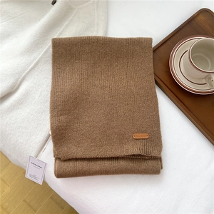 Detailed close-up of dark camel knit scarf texture with premium brand leather label