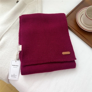 Close-up of wine red knitted scarf featuring a fine ribbed texture and a leather logo patch