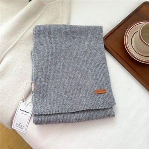 Detail of grey knitted wool scarf with brown leather tag and branding on a cozy tray