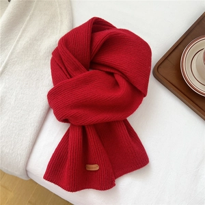 Detail of red chunky knit wool scarf featuring a premium leather logo tag on white background