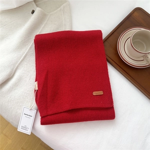 Close-up of deep red ribbed knit scarf with premium leather tag and brand label detail