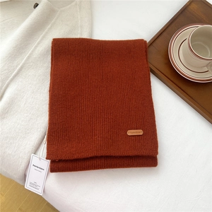 Detail of burnt orange knit scarf featuring vertical ribbed texture and leather brand label