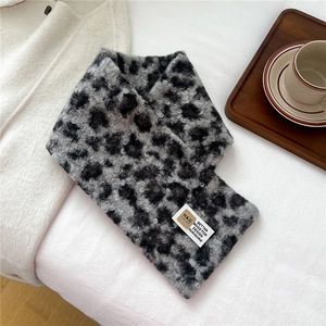 Detailed view of leopard print plush scarf with woven label on cozy white bedding