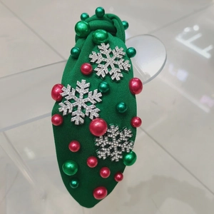 Detail of green knit headband with knot design, silver snowflakes and festive red pearls