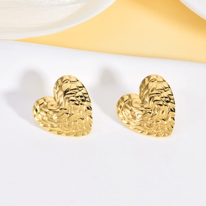 Detail of gold heart stud earrings with unique hammered texture and wavy surface design