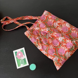 Detailed close-up of orange floral cotton tote bag with pink daisy patterns and straps
