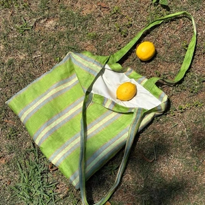 Green and blue striped cotton canvas tote bag with long straps on a natural grass background