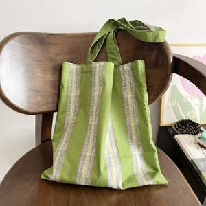 Detailed side view of a green and grey striped cotton canvas tote bag on a wooden chair