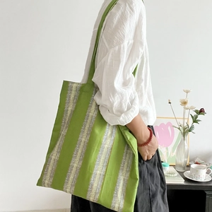Close-up of a green and white striped cotton tote bag worn over the shoulder by a model