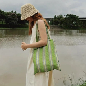 Outdoor shot of green striped cotton tote bag paired with a woven straw hat on a model