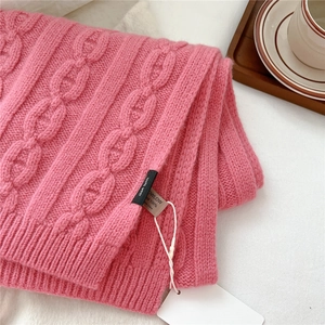 Détail d'une écharpe en laine rose à torsades avec étiquettes sur fond textile blanc