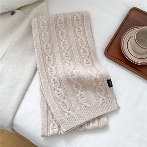 Détail d'une écharpe en laine crème avec motif torsadé et étiquette 100% laine