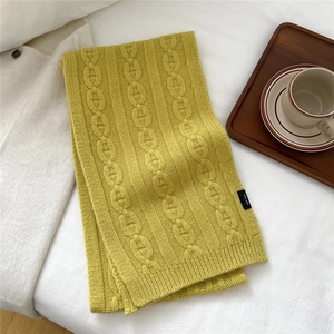 Détail d'une écharpe en laine jaune avec maille torsadée et étiquette 100% laine