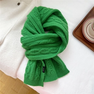 Détail d'une écharpe en laine vert vif avec tricot torsadé épais et étiquette de lavage