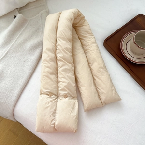 Detailed view of beige quilted down scarf with snap button closure on white cozy bedding